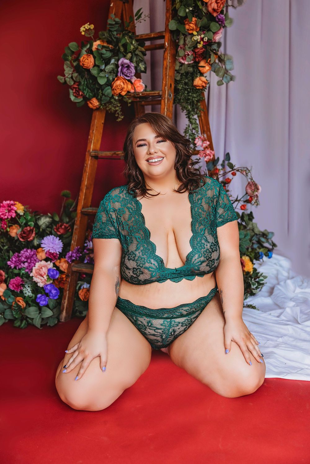 Plus size boudoir photo with teal lace lingerie against floral backdrop.