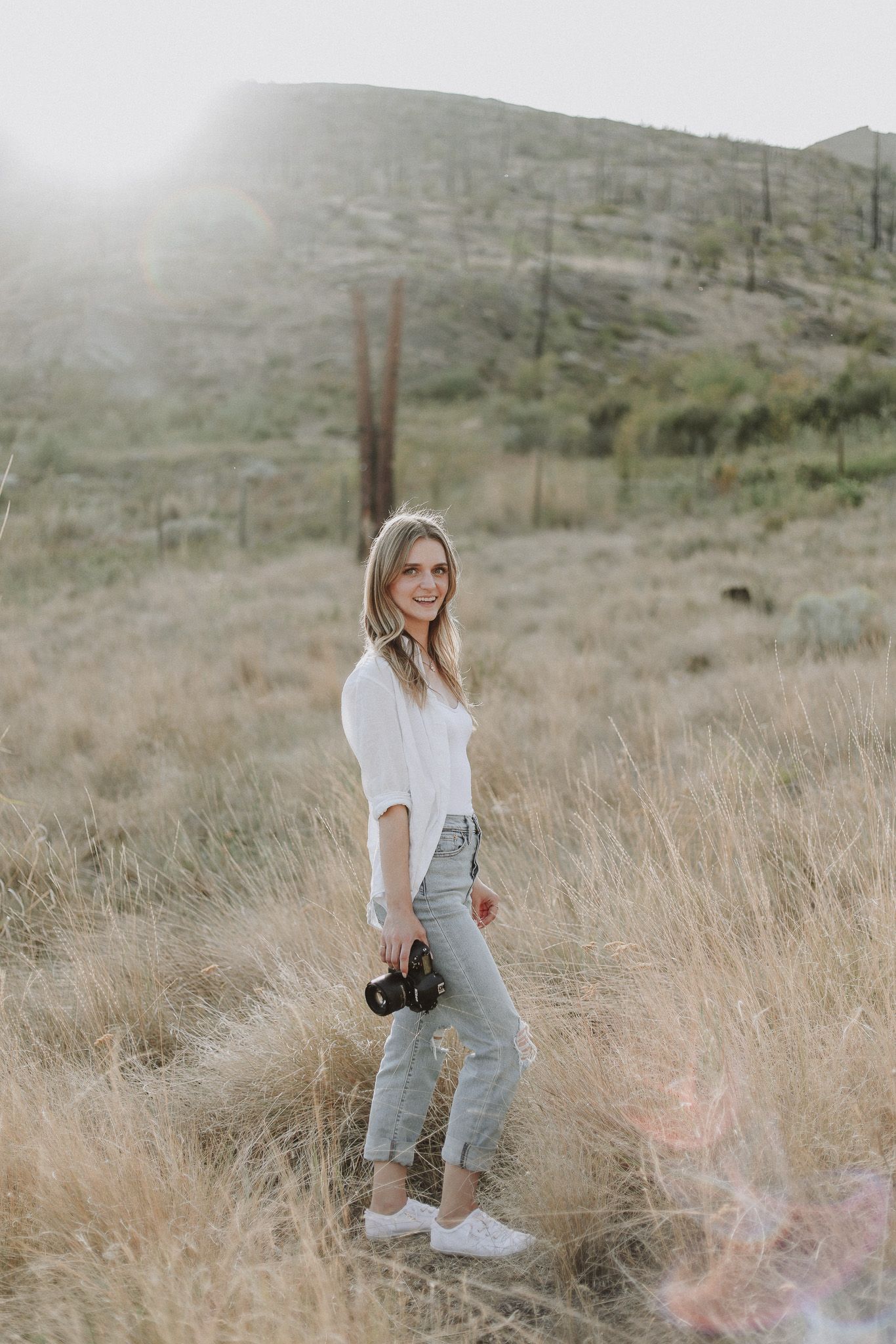 A photographer stands in a misty mountain field holding camera equipment.