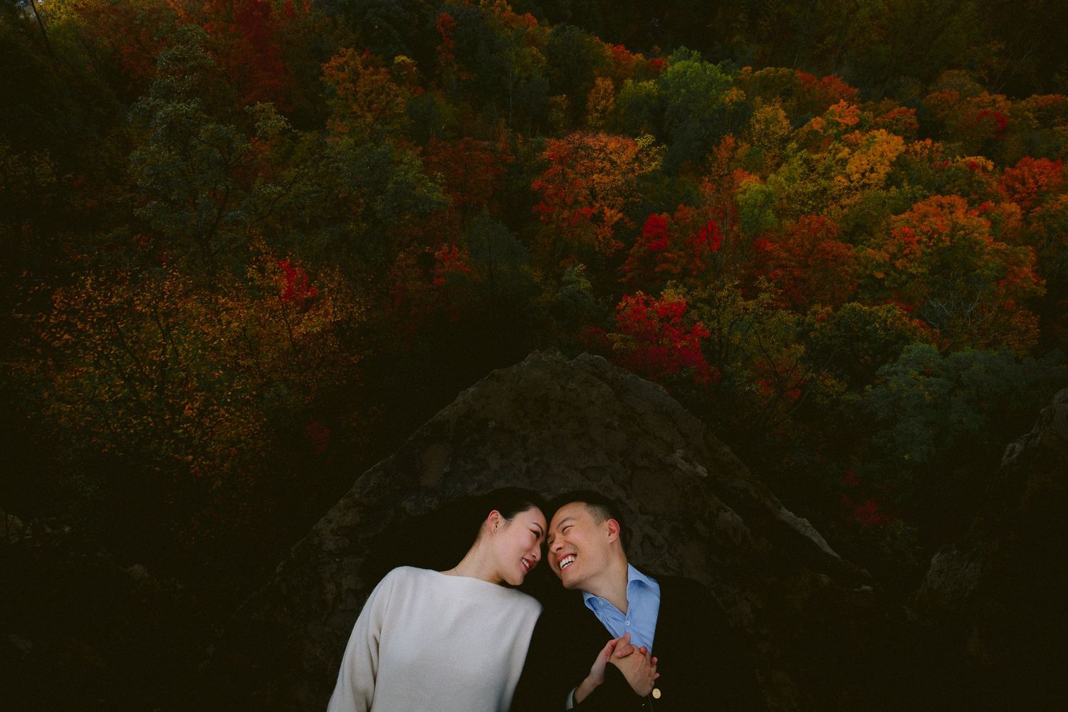A couple shares an intimate moment against backdrop of vibrant autumn foliage at dusk.