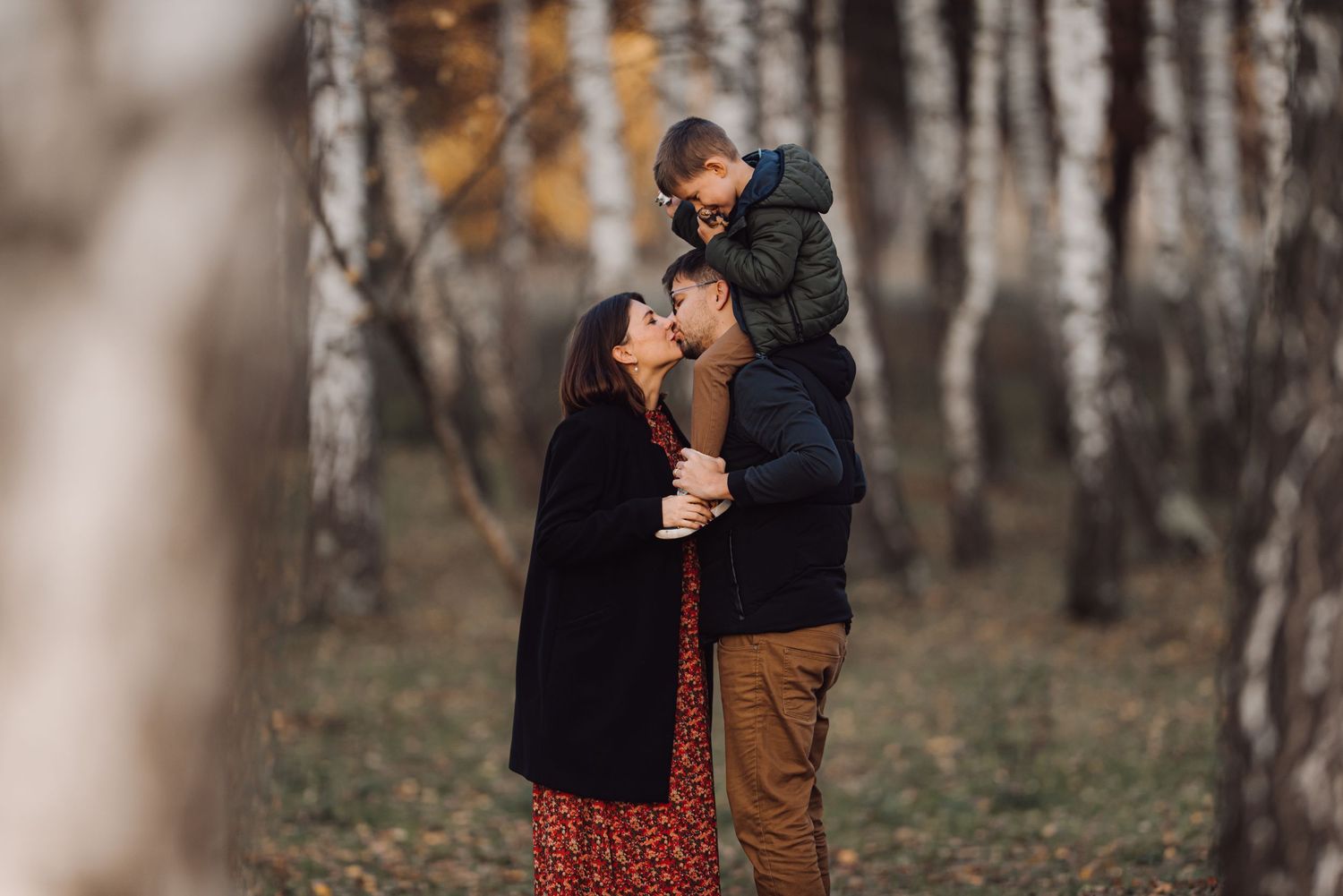 A romantic autumn scene in a birch forest with a couple and child sharing an intimate moment together.