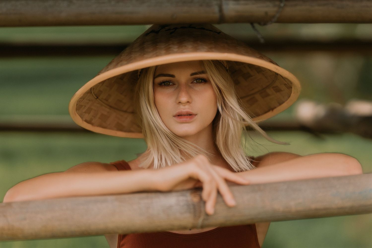 Person wearing a wide-brimmed straw hat leaning on a wooden railing in natural light.