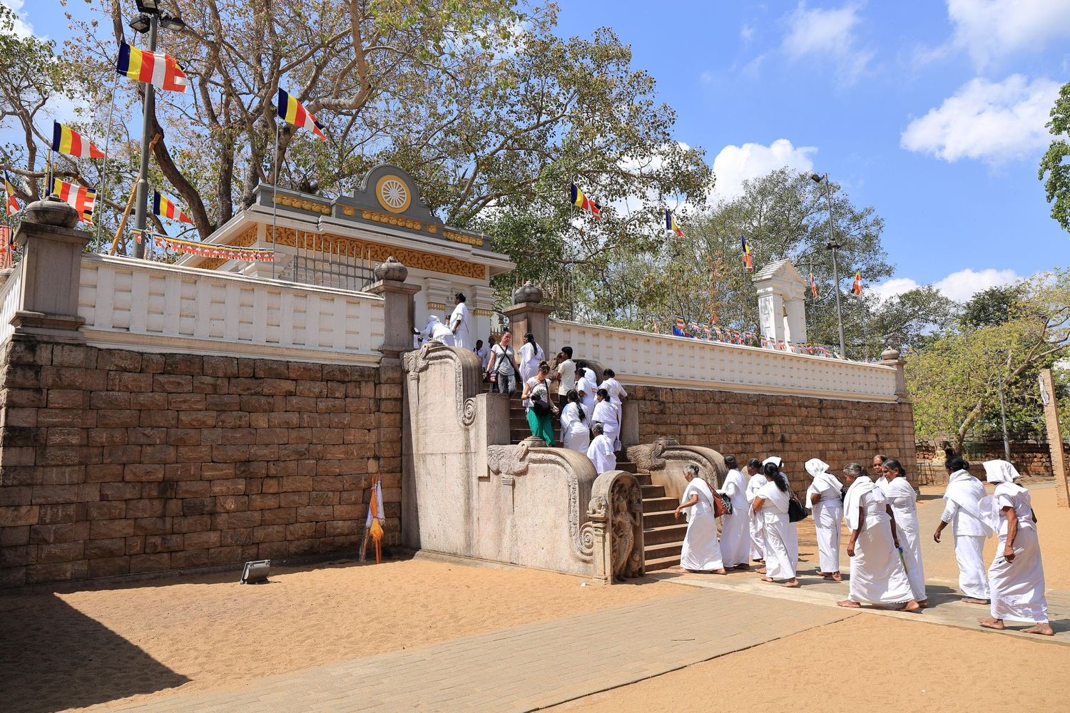 People in white clothing ascending stone steps at a Buddhist temple entrance.