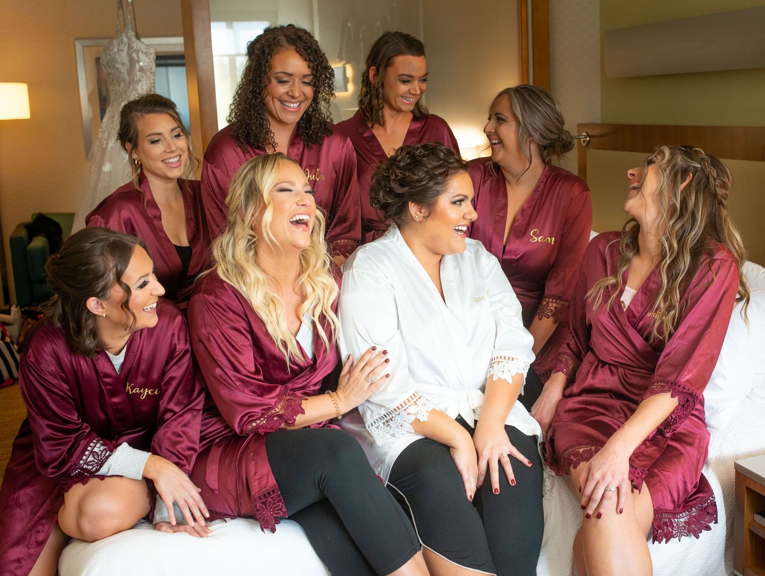 Wedding party in burgundy robes sharing laughter during pre-ceremony preparations.