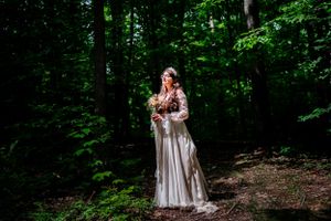 A solitary figure in a flowing white dress stands among lush green forest trees.