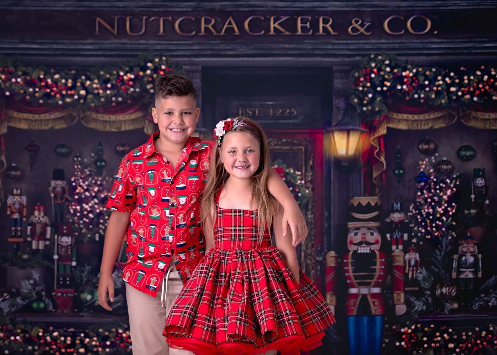 child brother and Sister in Christmas theme apparel smiling at the viewer while standing in front of a Nutcracker store.