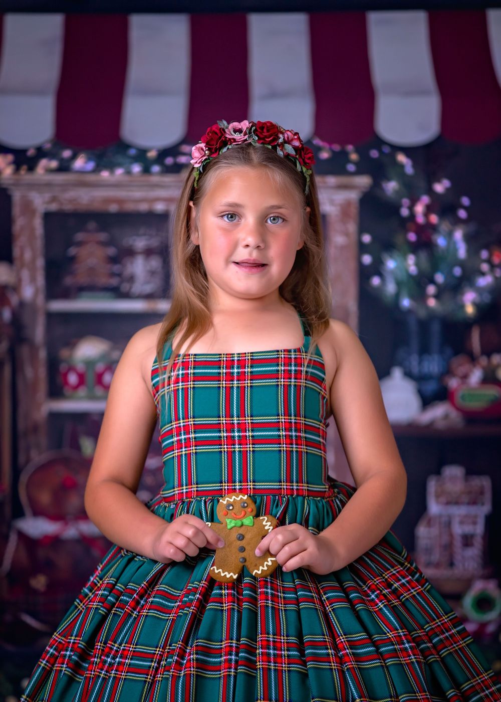 Girl standing in front of Gingerbread store studio backdrop wearing a green tartan gown holding a gingerbread cookie