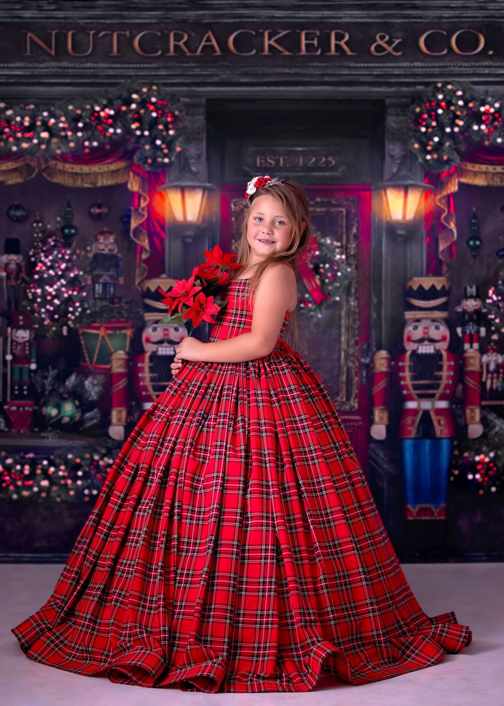 Girl standing in front of Nutcracker store studio backdrop wearing a long red tartan gown and holding poinsettia flowers