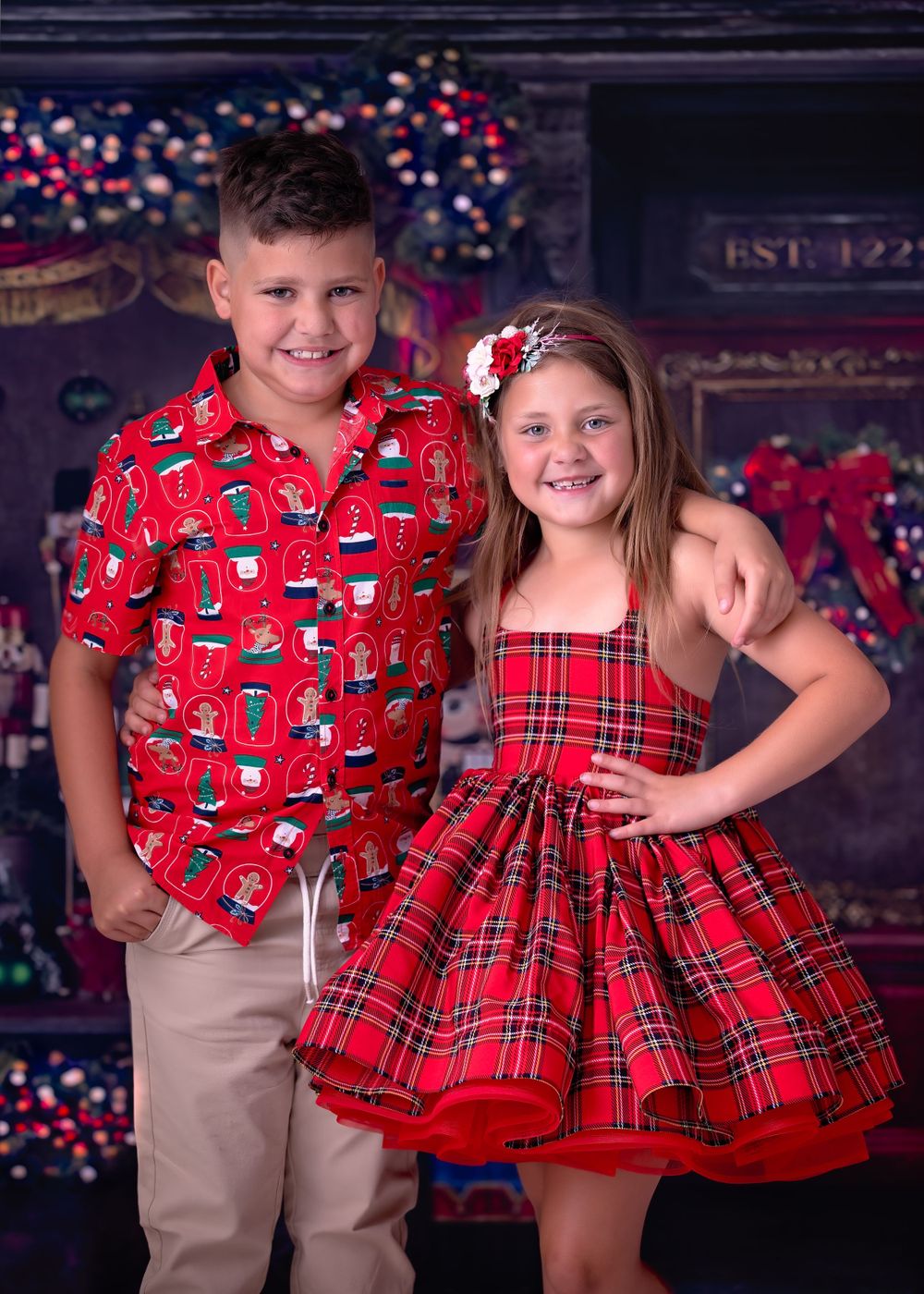 child brother and Sister in Christmas theme apparel smiling at the viewer while standing in front of a Nutcracker store.