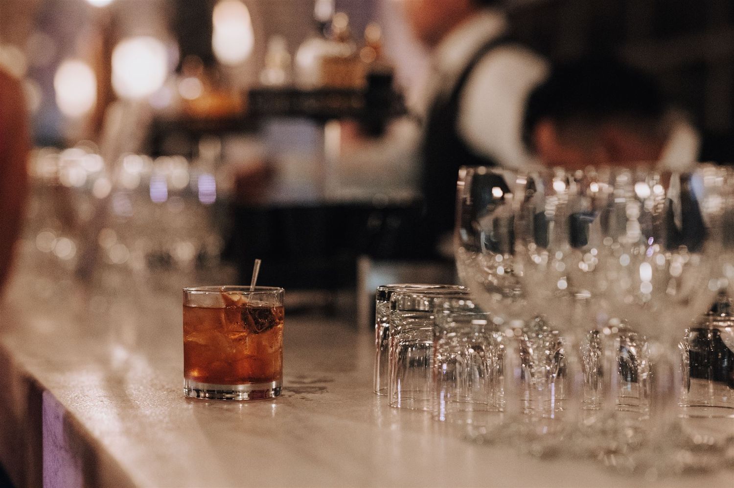 Cocktail bar setup with glasses and an old fashioned drink in warm ambient lighting.