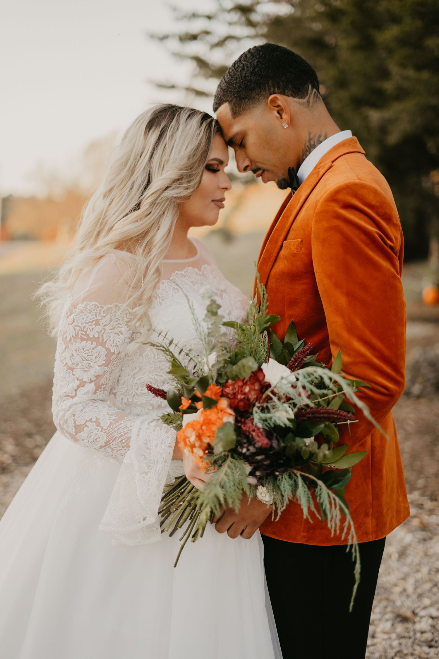 Wedding couple sharing intimate moment with vibrant orange jacket and white lace dress.