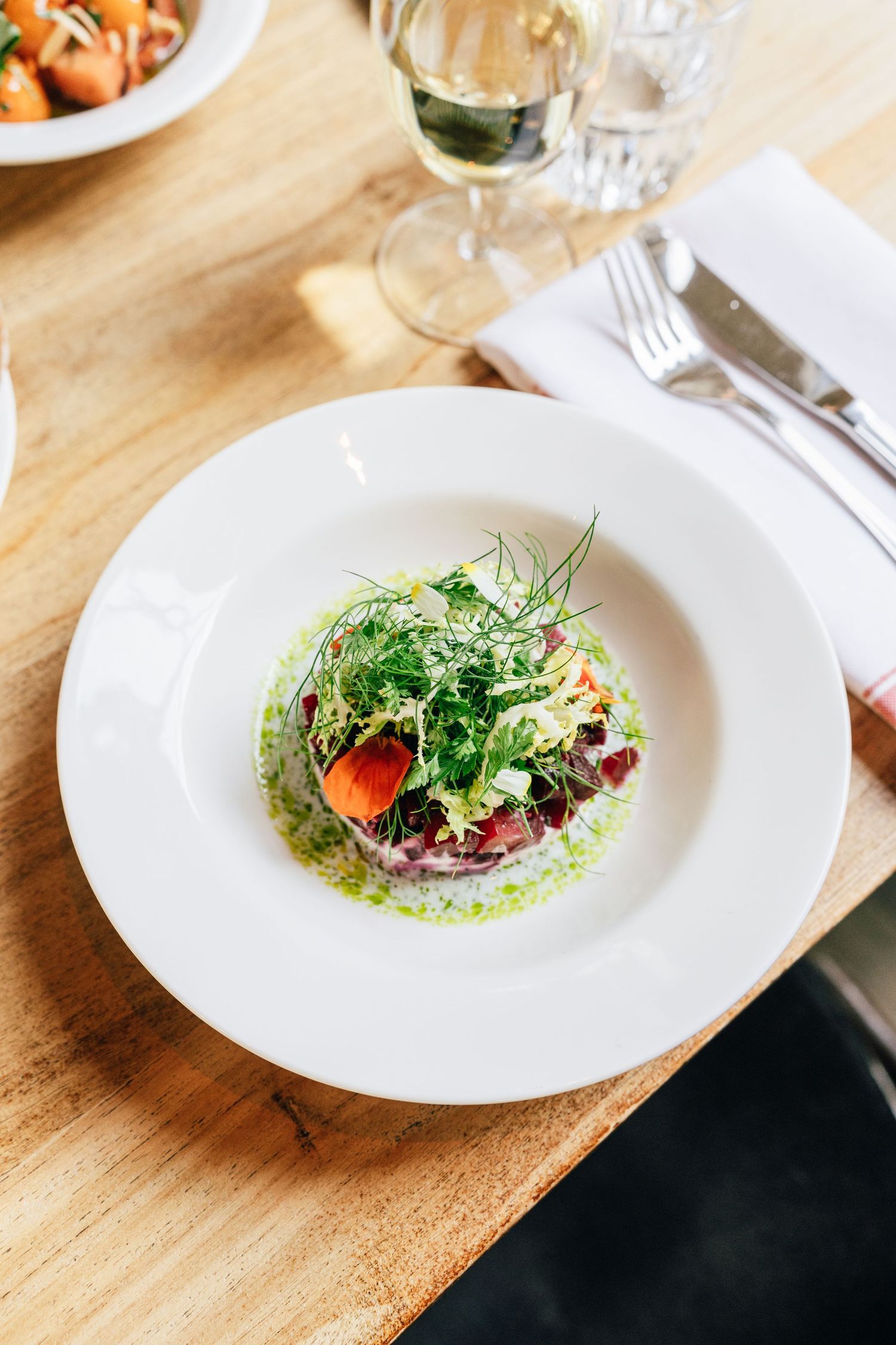 Fresh green salad with microgreens and edible flowers plated elegantly on a white dish with wine pairing.