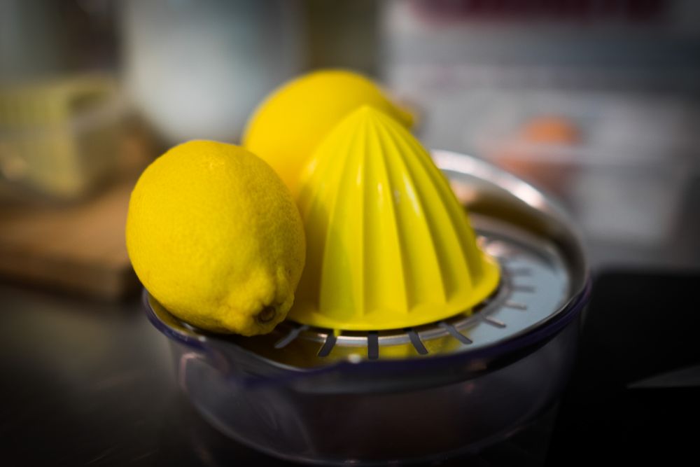 Two fresh yellow lemons resting on a stainless steel citrus juicer on a kitchen counter.