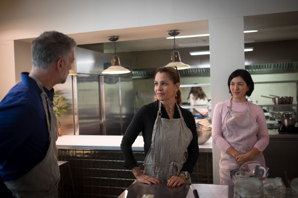 Three people in aprons having a conversation in a professional restaurant kitchen.