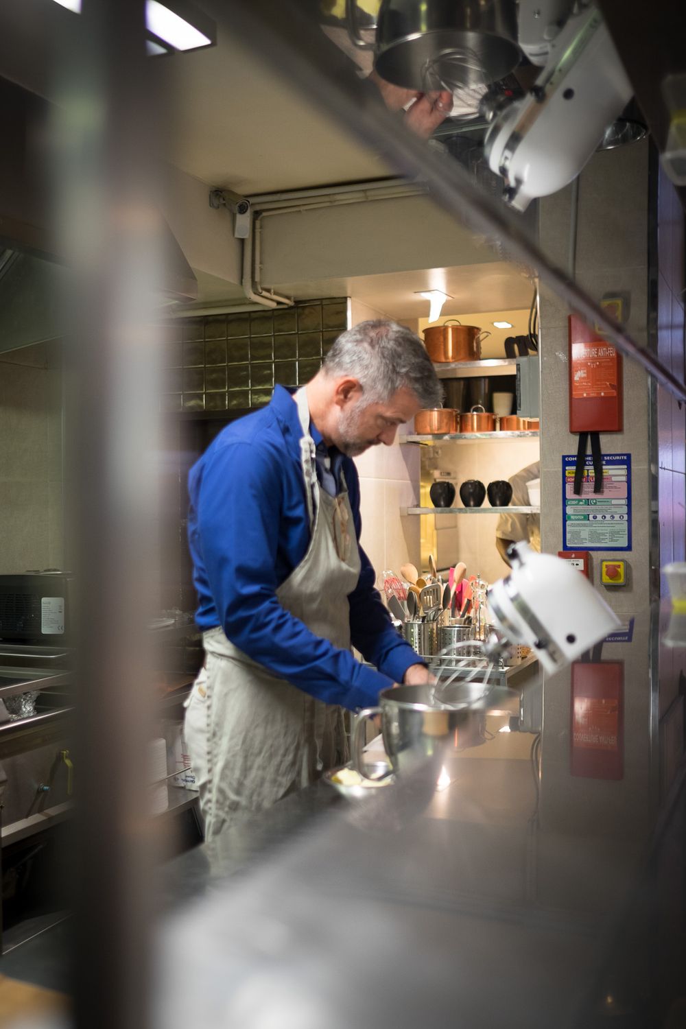 Male chef in blue shirt and apron working at a stainless steel counter in a professional kitchen.