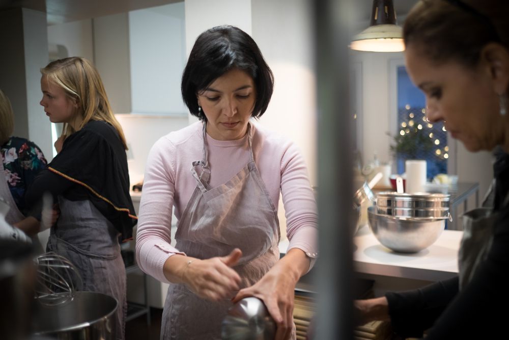 Woman in pink apron mixing ingredients in a bowl during a cooking class in a modern kitchen.