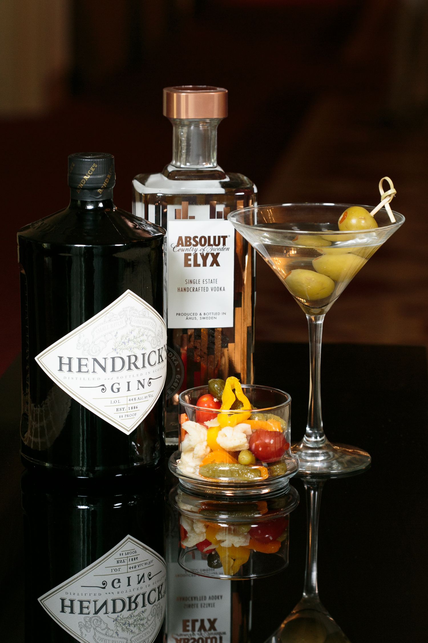 Elegant cocktails with garnishes displayed next to Hendricks gin bottles in dark lighting.