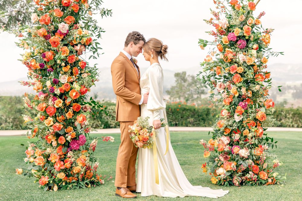 Bride and groom sharing intimate moment between two tall vibrant orange and pink floral ceremony columns.