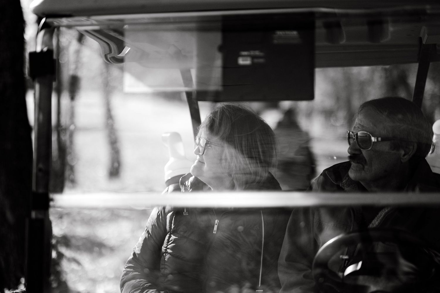 Black and white image of a man and woman wearing sunglasses while sitting in a golf cart watching golf