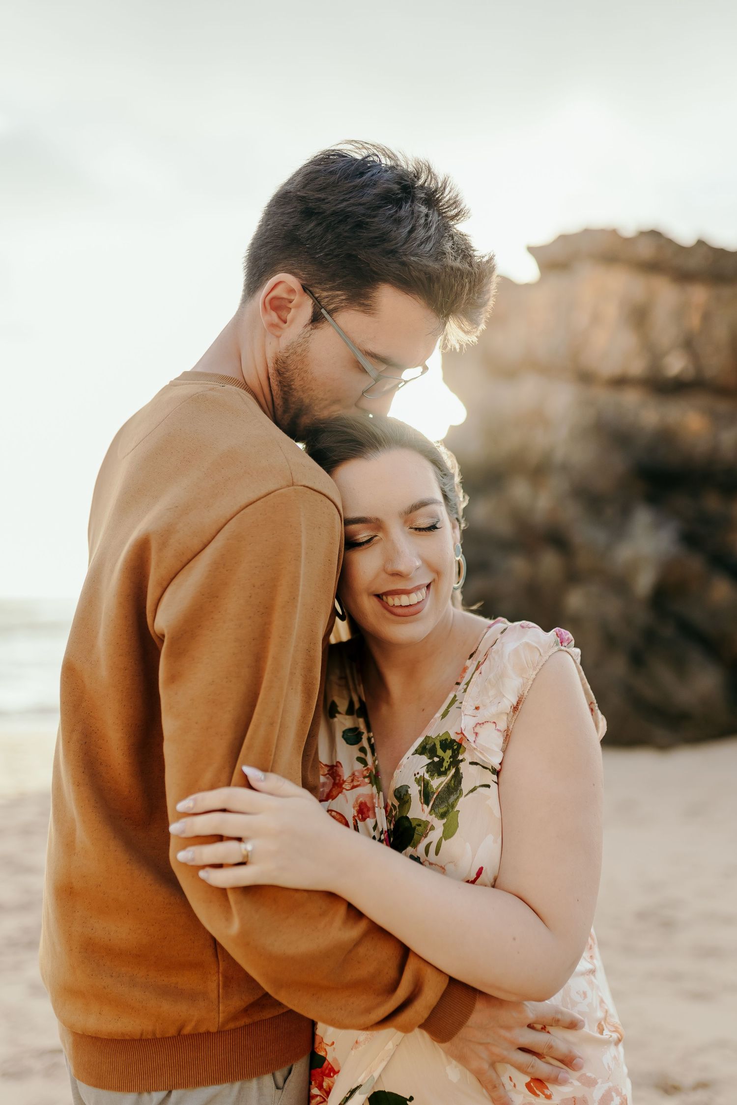 Couple sharing tender embrace on beach with warm golden sunset light.