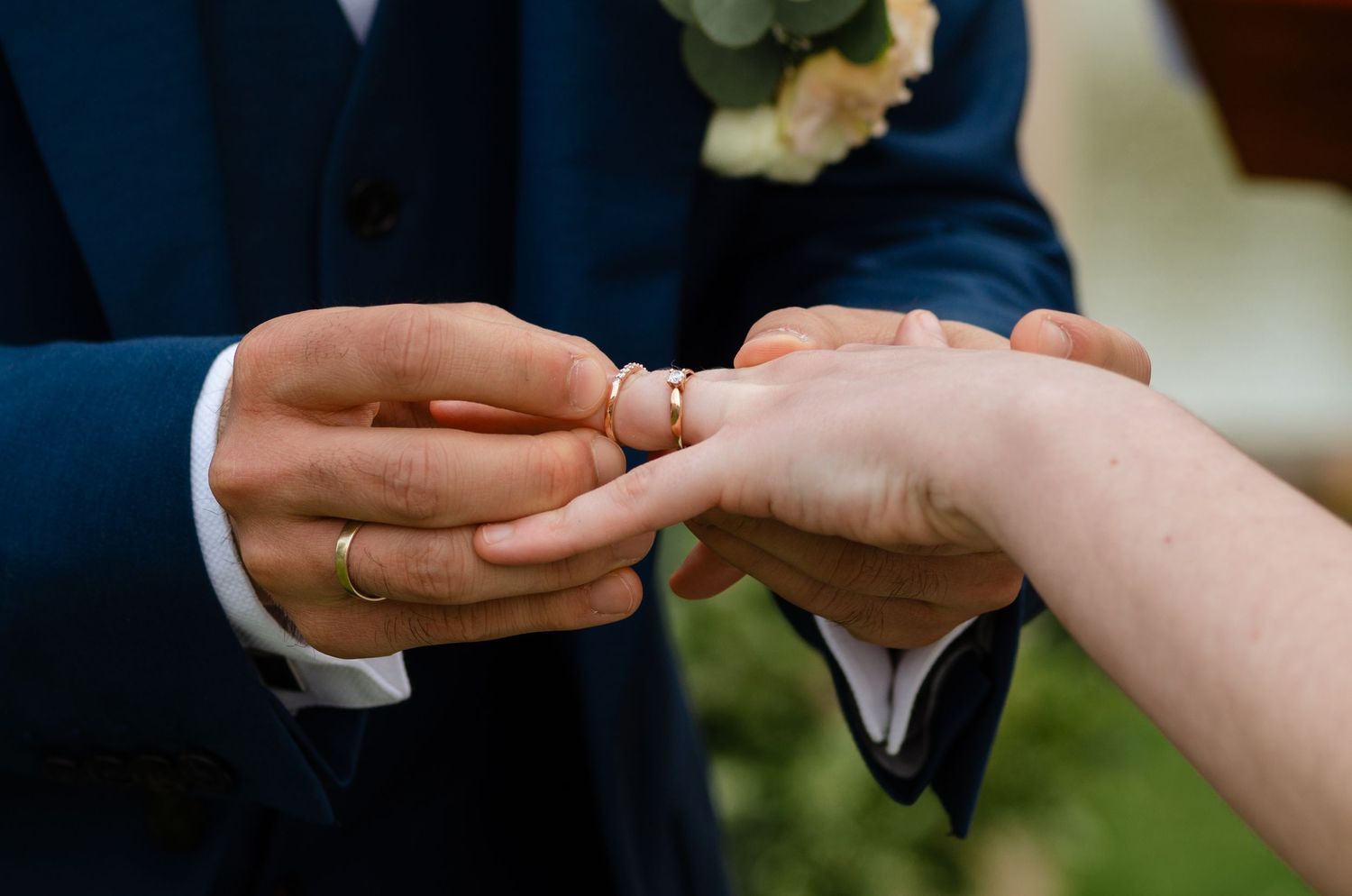 Hands exchanging wedding rings during ceremony with delicate floral details.