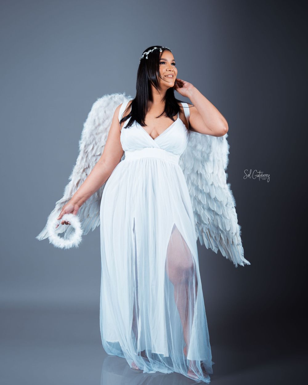 Fine art studio photoshoot in Allentown PA of woman in white dress with angel wings holding halo prop.