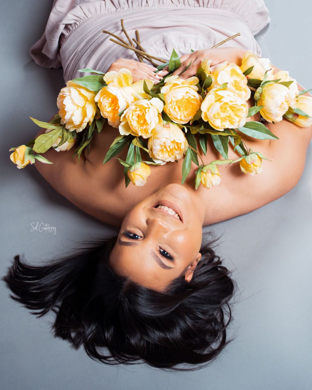 Stylish portrait photography in Allentown PA of woman lying with yellow flowers on soft studio background