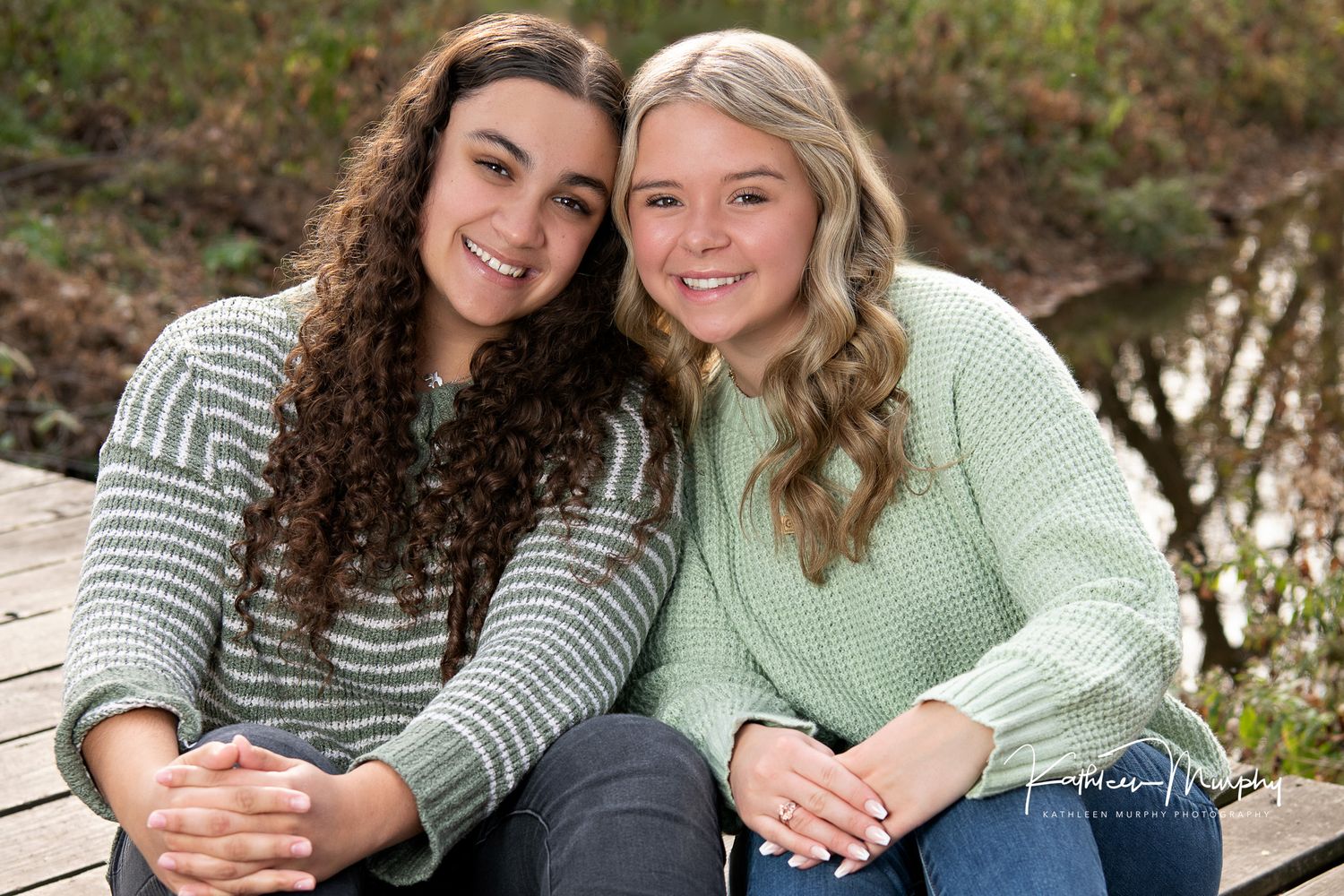 Two friends in matching sweaters sitting together outdoors.