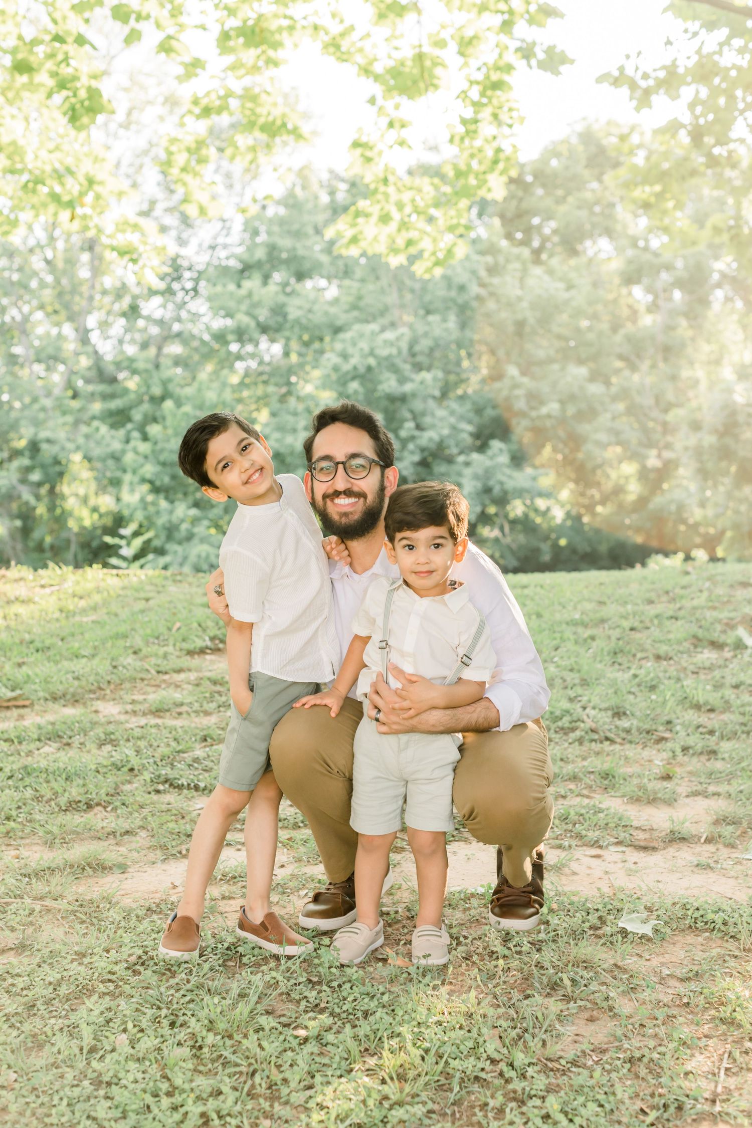 Three people share playful embrace while posing on grassy slope in coordinated outfits.