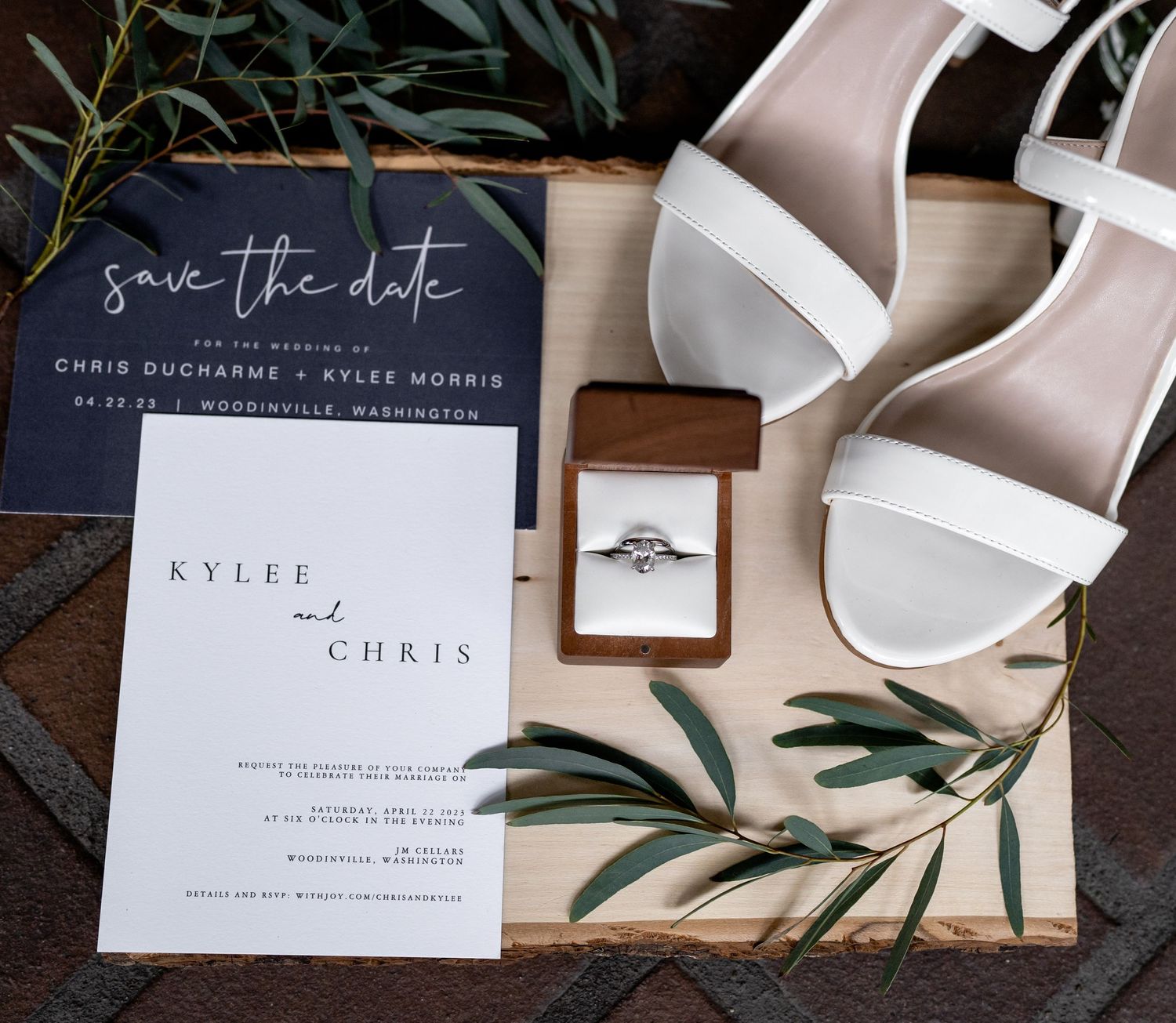 Wedding details flatlay with save the date cards, white sandals, and engagement ring in wooden box.