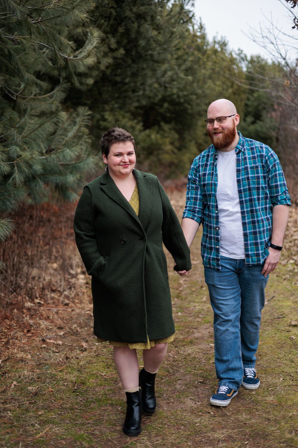 A couple walks hand in hand along a nature trail during their engagement photo session.