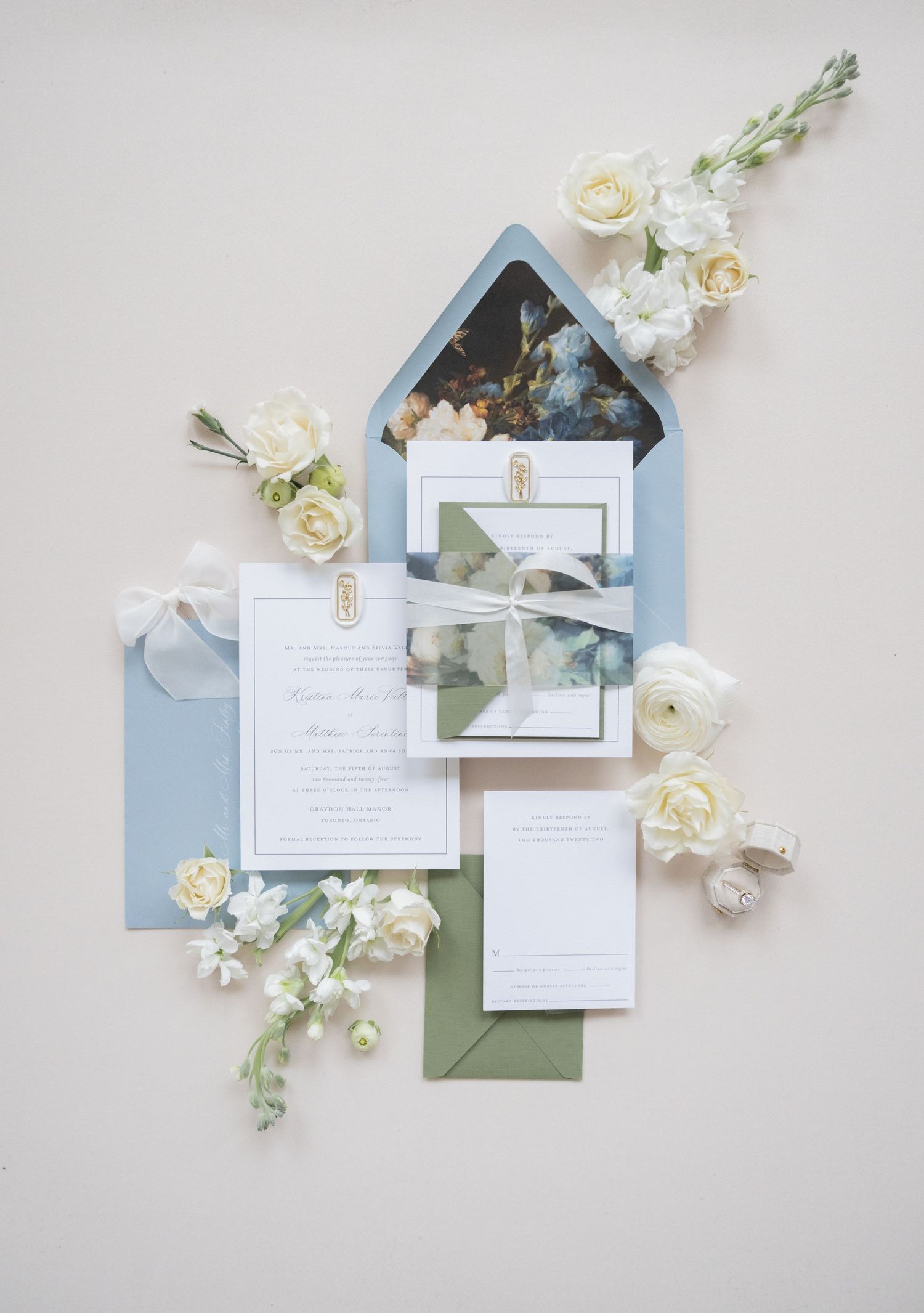 Wedding invitation suite with dusty blue envelopes and white roses arranged on light gray background.