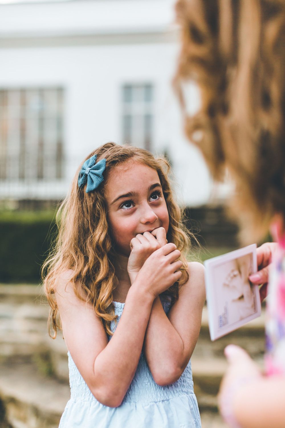 A child in a blue dress reacts with surprise and joy while covering their mouth.
