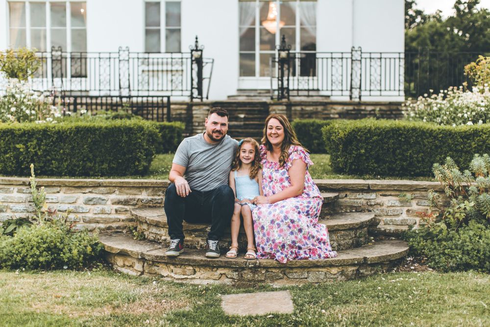 Family seated together on stone garden steps with white building in background.