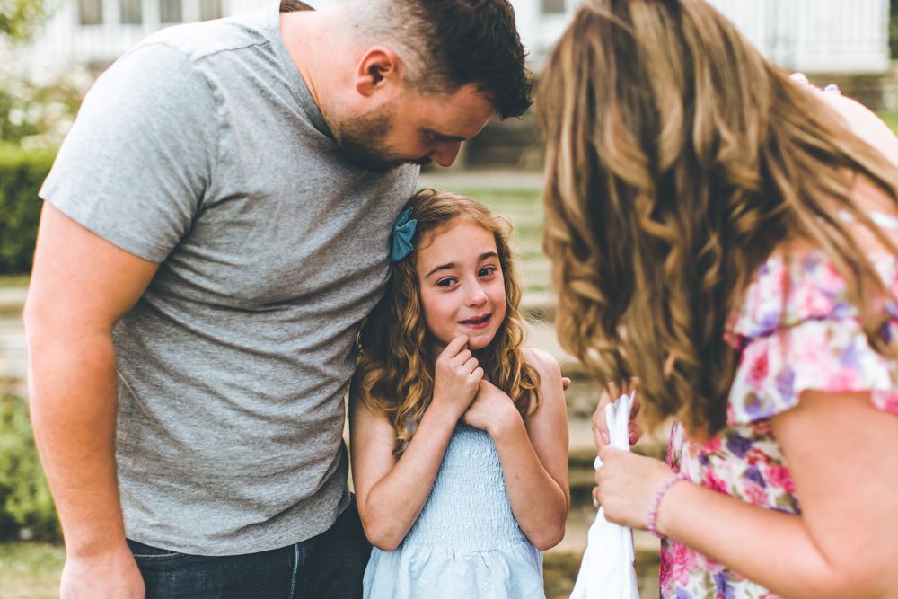 Three people embrace in front of a white house during a special moment.