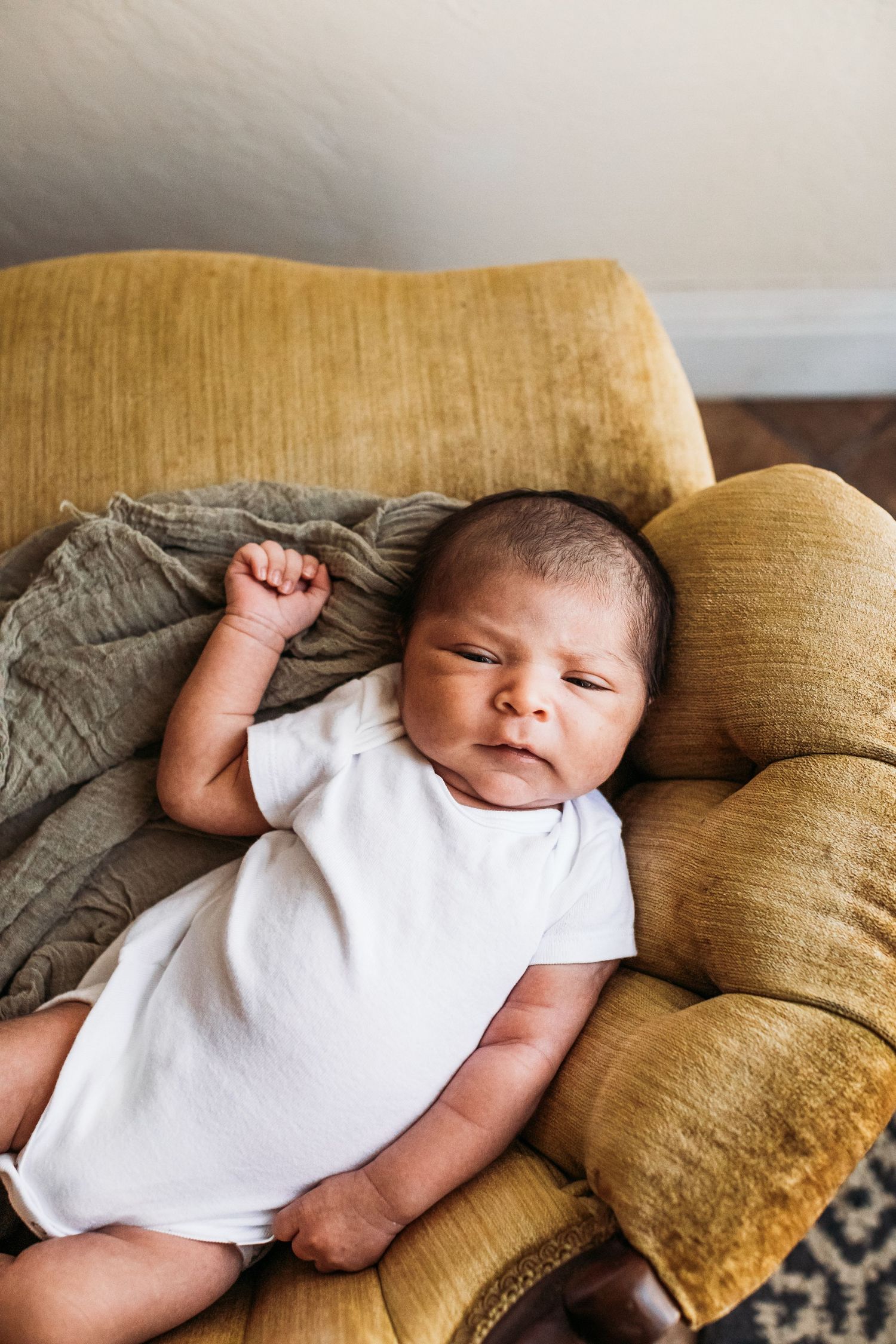 Peaceful baby sleeping on yellow velvet couch with gray blanket.