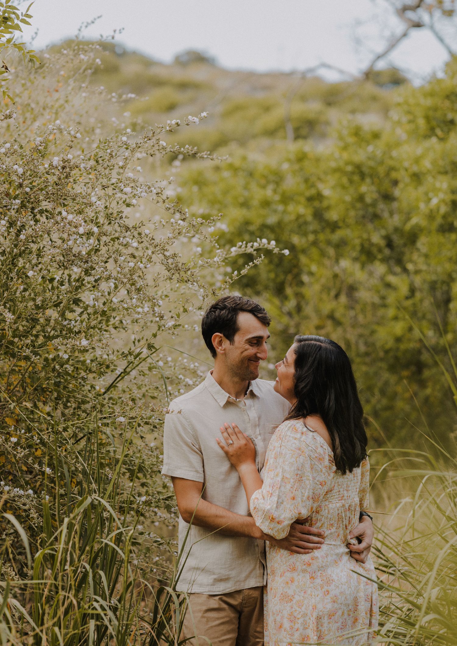 sweet moment of couple smiling at each other intimately in front of a blurred flowers and greenery
