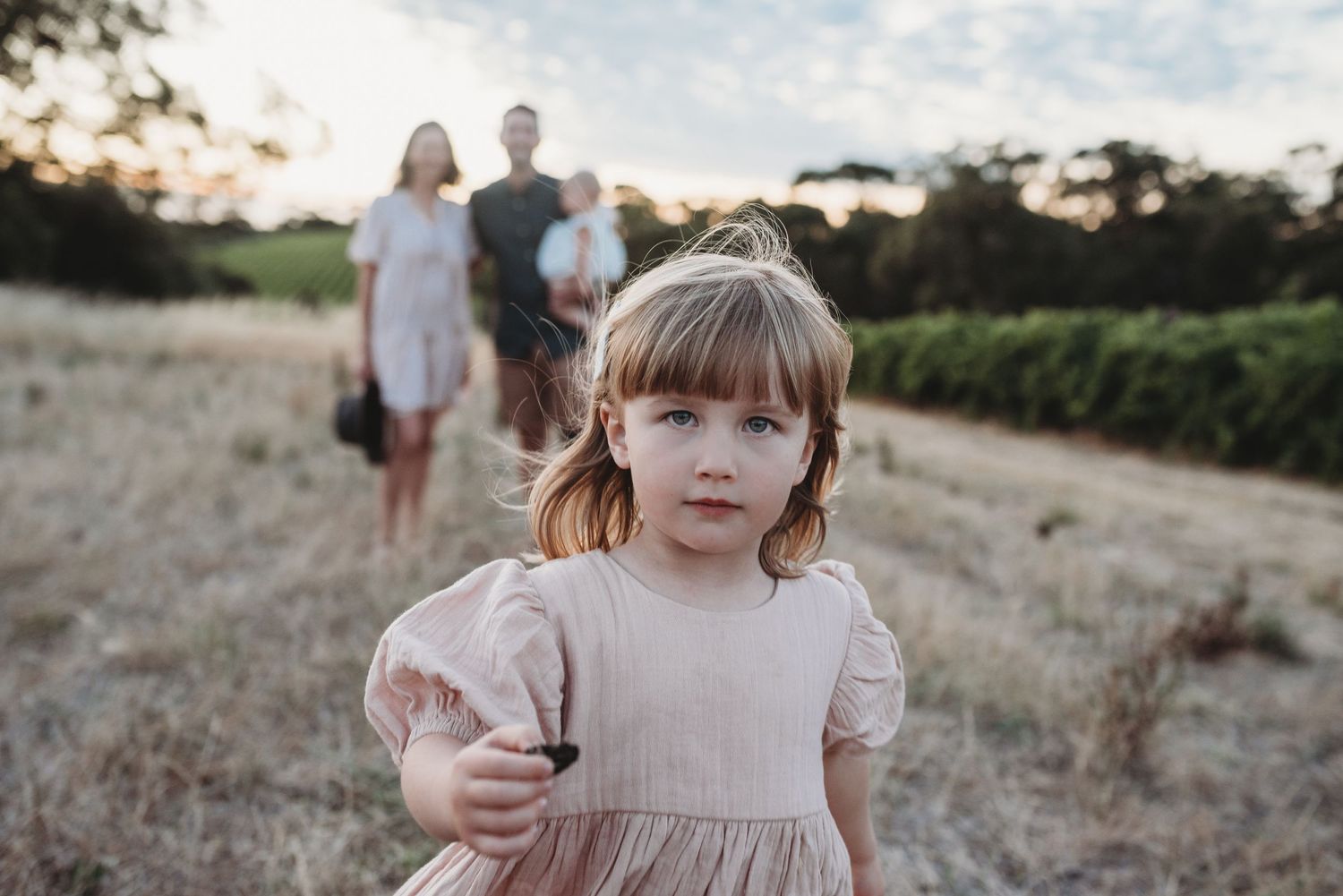 Young girl in pink dress standing in field during golden hour.