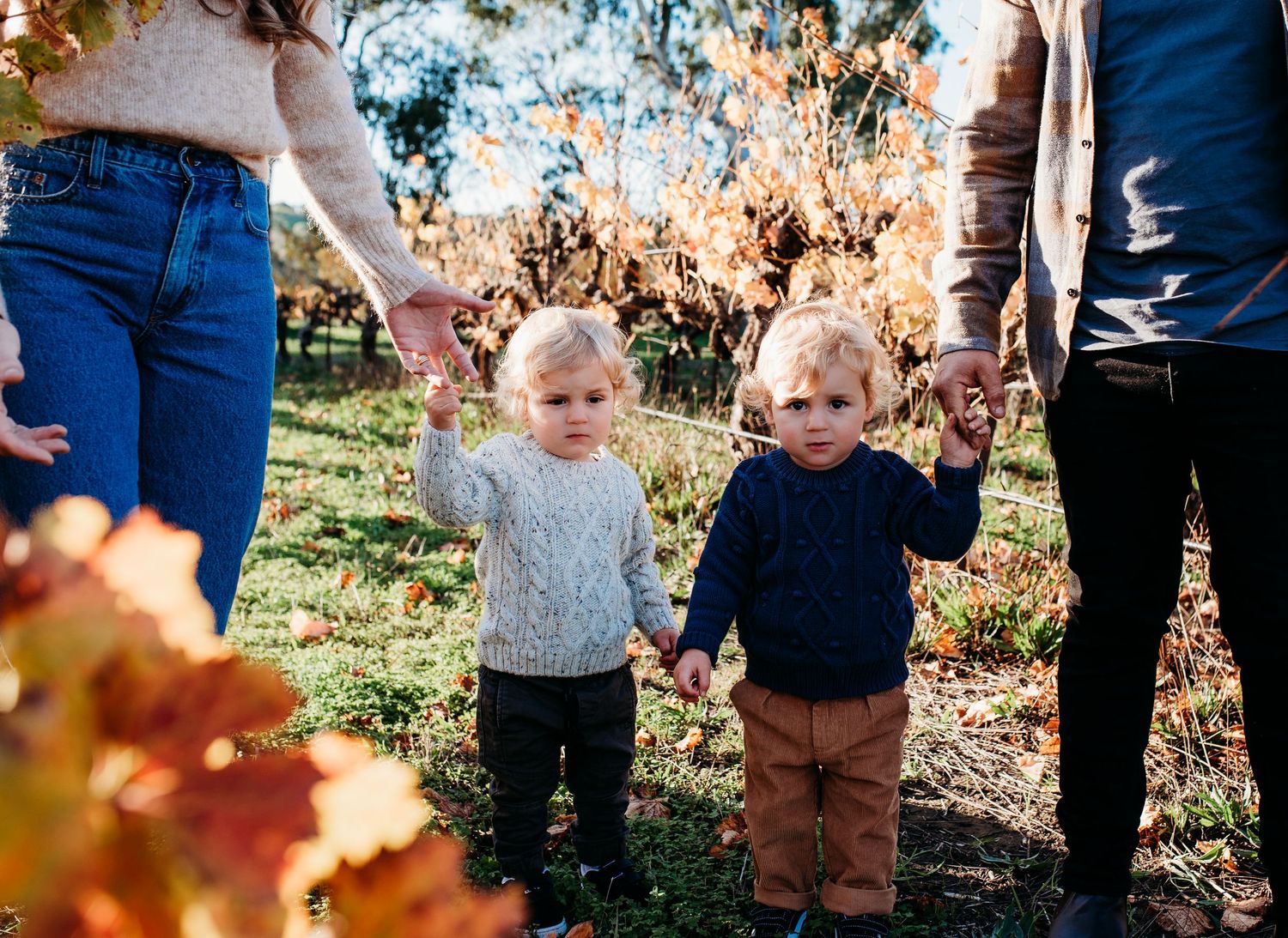Family members' legs and feet shown walking through autumn foliage.