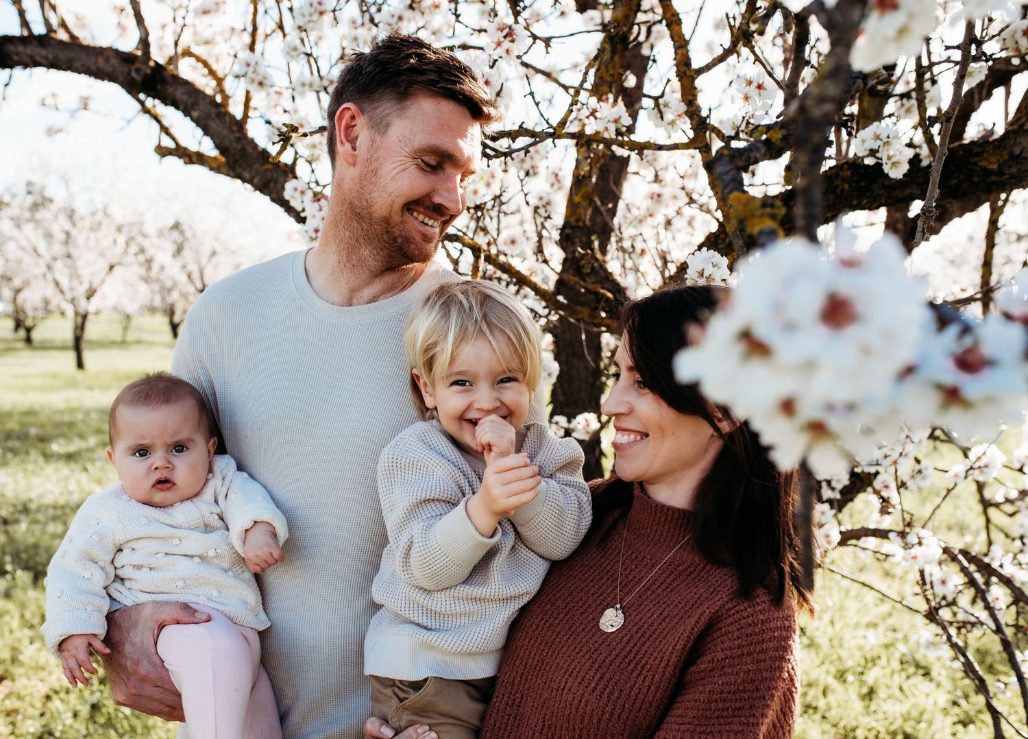 Family portrait taken among blooming trees in an orchard setting.