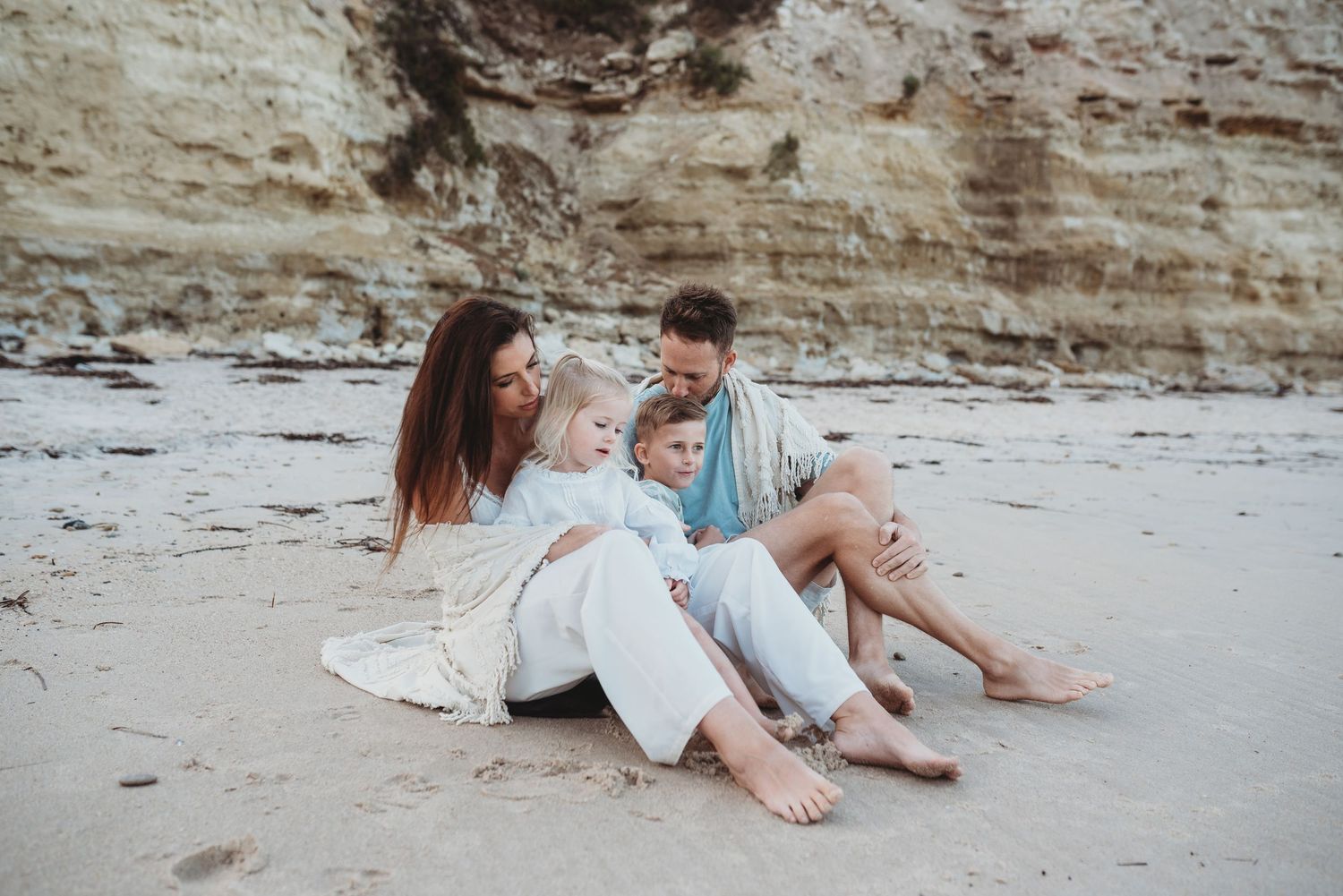 Romantic beach photoshoot with couple lounging on sand near coastal cliffs.