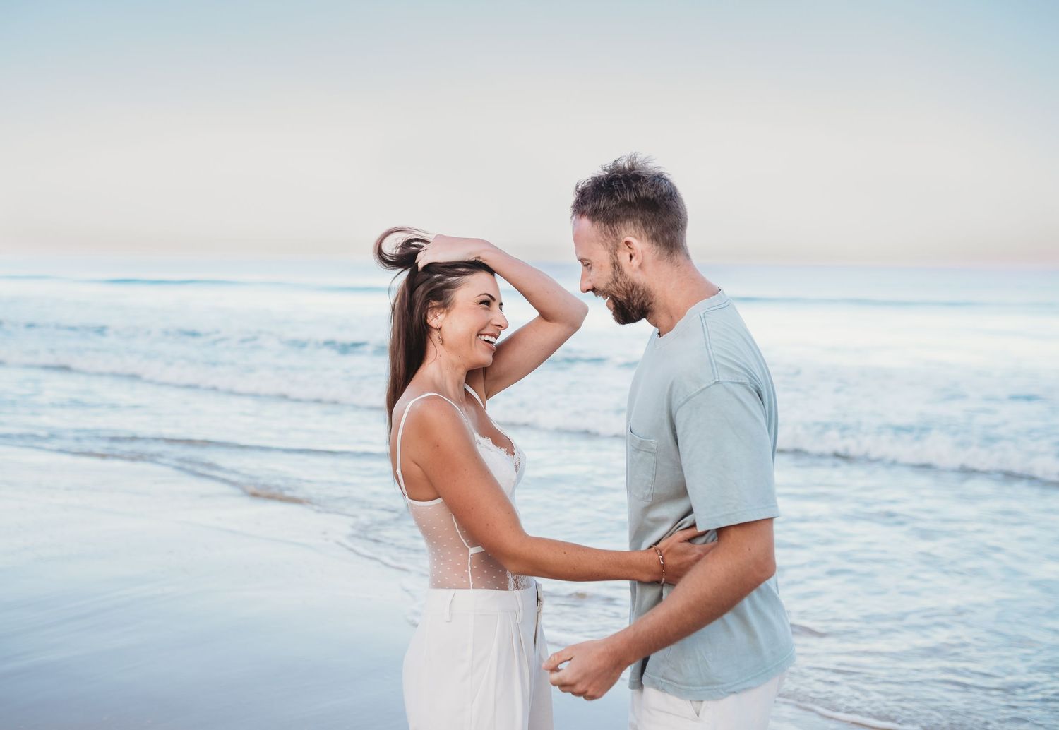 Couple sharing joyful moments on beach with ocean waves in background.