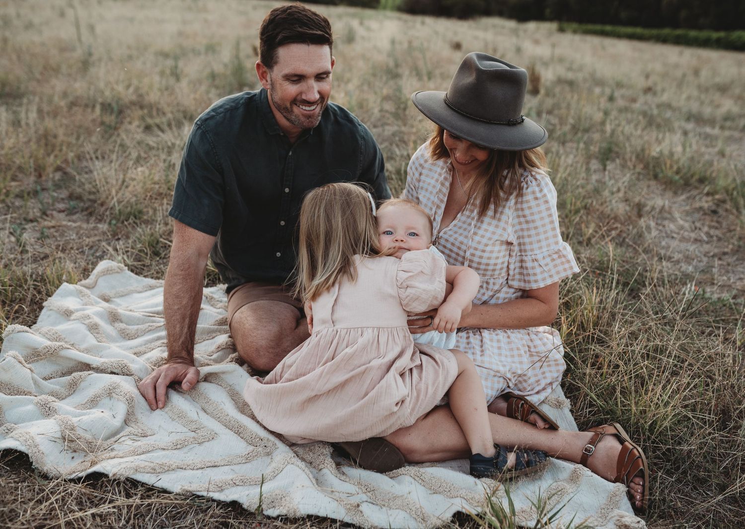 Family sitting together on blanket in field during golden hour.