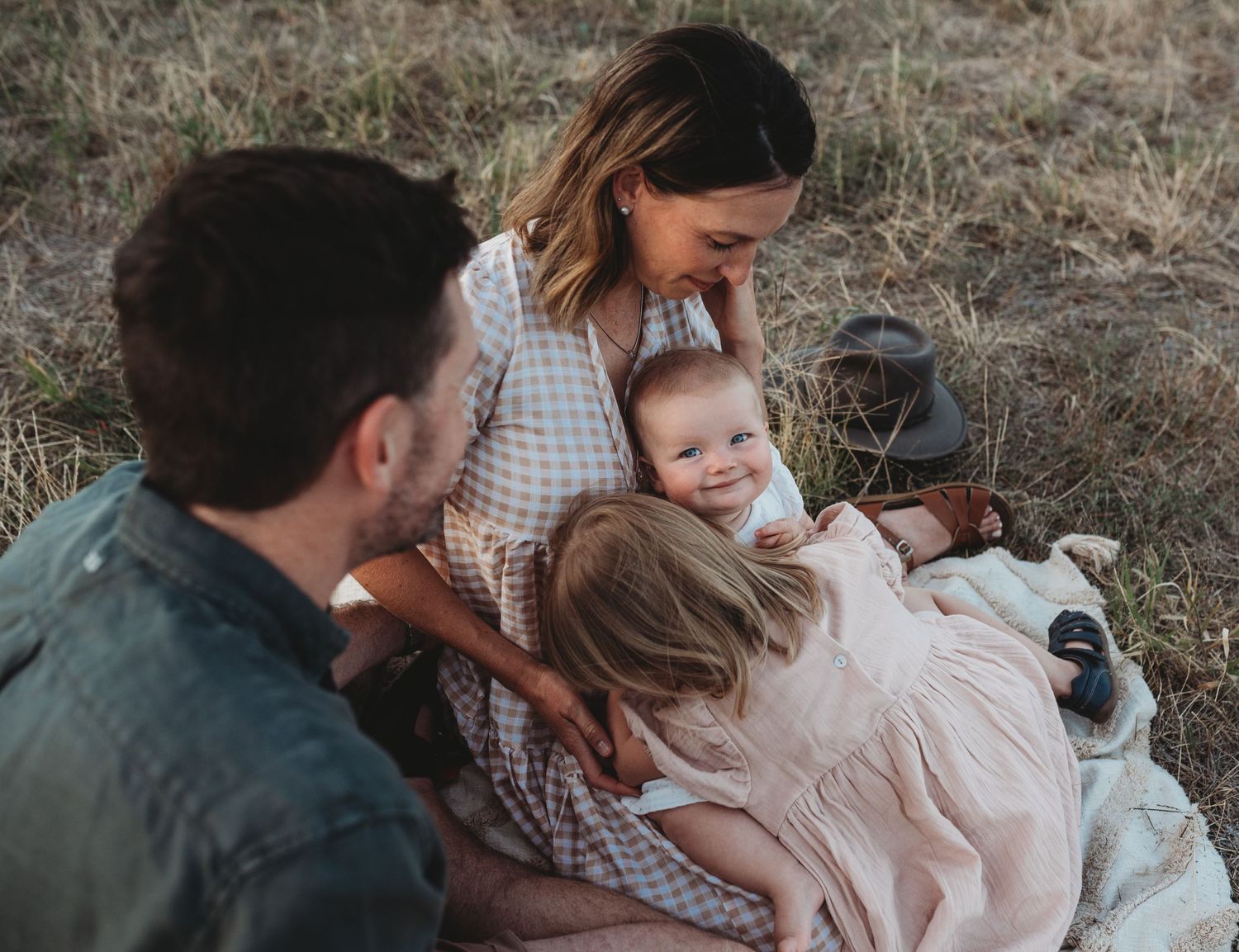 Family sharing intimate moment while sitting on blanket outdoors.