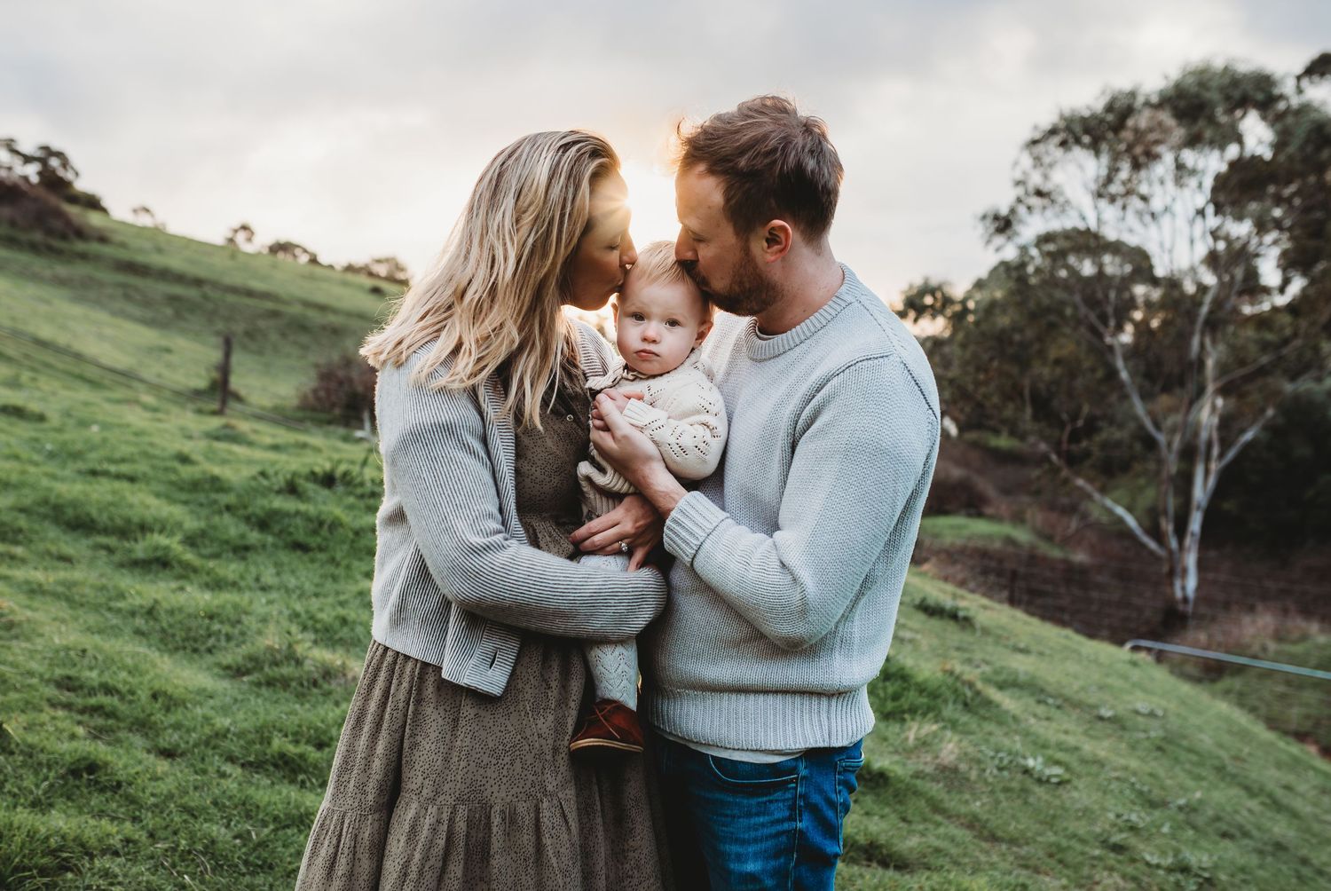Intimate outdoor family moment against a pastoral hillside backdrop.