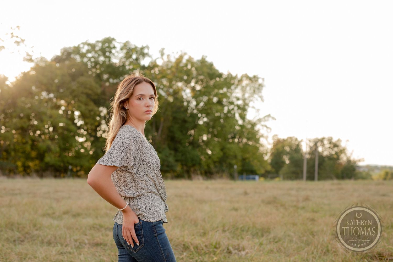 Natural lifestyle portrait in gray top against sunset lit meadow.