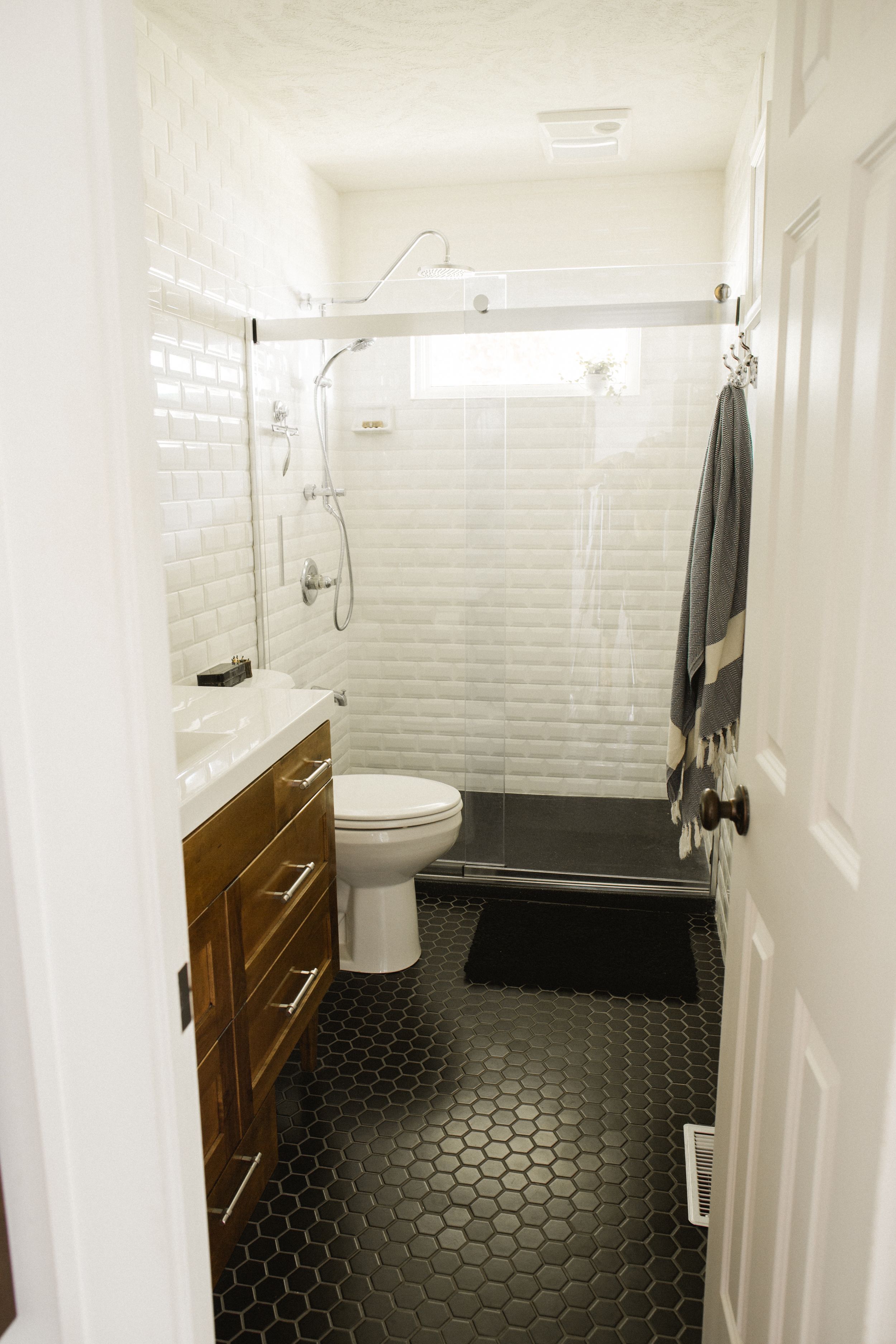 Modern bathroom with black hexagon floor tiles, white subway tile walls, and wooden vanity cabinets.