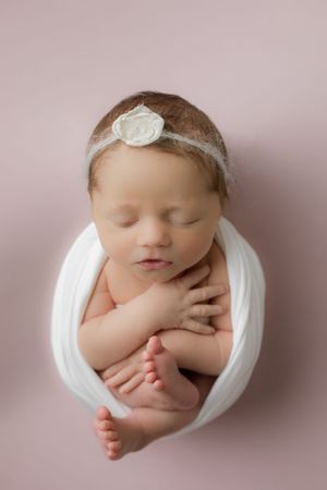 Pink background blanket with a baby girl swaddled in white for her newborn photoshoot at the studio.