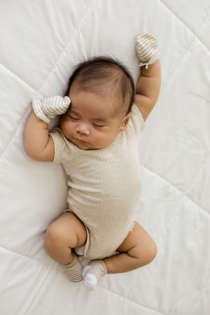 A lifestyle newborn portrait of a sweet sleeping baby laying on the bed in the white studio bedroom for his newborn photoshoot.