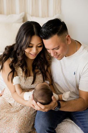 A close up photo of a mom and dad looking down at their precious newborn baby and smiling in the bedroom studio setup.
