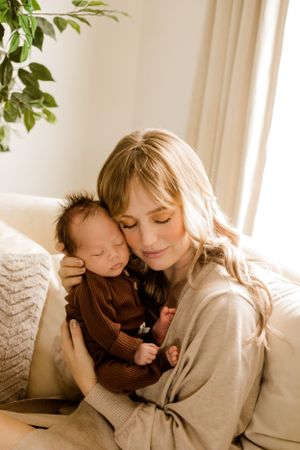 Mom snuggles newborn baby close to her face in the comfort of her own living room during her lifestyle newborn session.